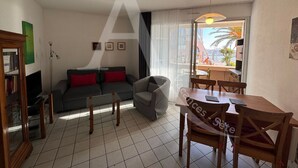 A living room with a grey sofa, red cushions, a grey armchair, a wooden dining table with chairs, and a bookshelf. - CONFORTABLE T2 AVEC PKG SETE PORT DE PLAISANCE (Sète)