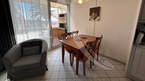 A dining area with a wooden table and chairs, a grey armchair, and a pendant light. - CONFORTABLE T2 AVEC PKG SETE PORT DE PLAISANCE (Sète)