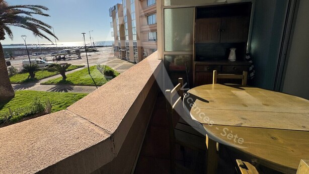 A balcony with a view of the sea, a wooden table, and a kitchen area with cabinets and a sink. - CONFORTABLE T2 AVEC PKG SETE PORT DE PLAISANCE (Sète)