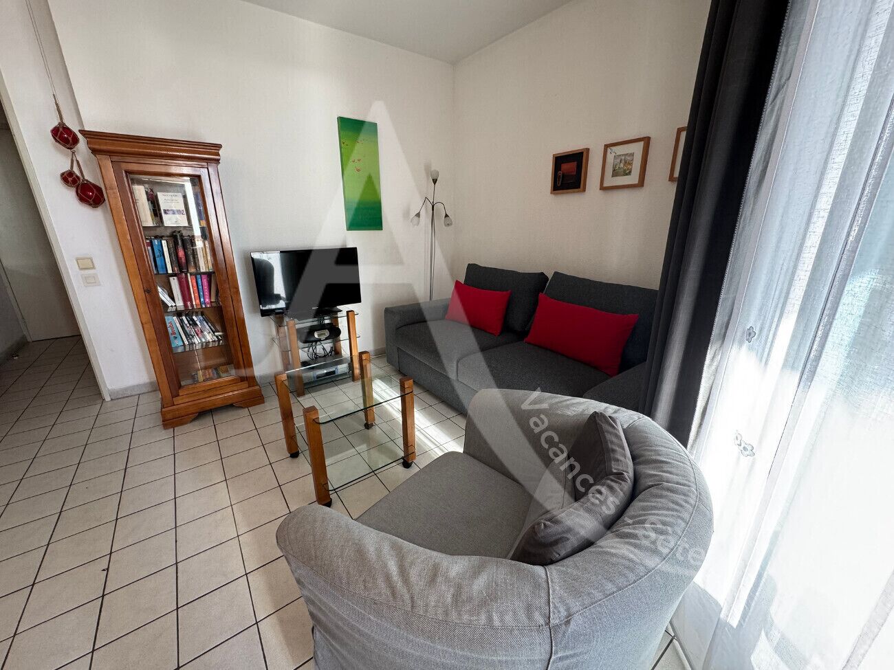 A living room with a grey sofa, a wooden bookshelf, a flat-screen TV, and a floor lamp.