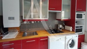 Una cocina compacta con gabinetes rojos, lavavajillas integrado, microondas y lavadora.