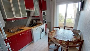 Cocina compacta con armarios rojos, lavadora y comedor con mesa y sillas.