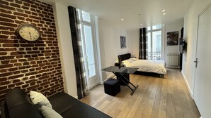 Um apartamento moderno com parede de tijolos, um sofá preto, uma mesa de jantar, duas camas e janelas amplas.