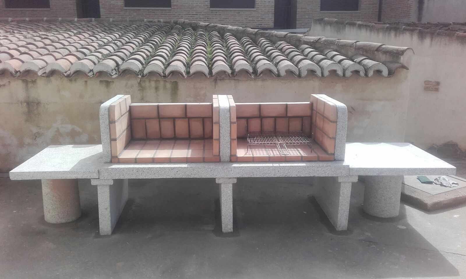 A concrete bench with a metal grill in the center, set against a wall with a tiled roof.