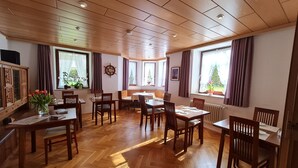 En matplats med trägolv och bord, stora fönster med gardiner och ett träpanelat tak med infälld belysning.