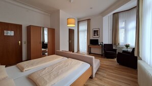 Ett hotellrum med en stor säng, ett skrivbord med en dator, en stol och ett fönster med gardiner.