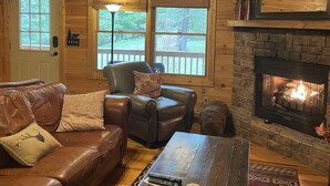A cozy cabin interior with a leather sofa, a stone fireplace, and a ceiling fan. - Beautiful Custom Cabin on almost 2 acres with lots of privacy (Blue Ridge)