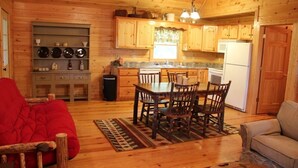 A cozy cabin interior with a wooden dining table, chairs, a sofa, and a kitchen area with wooden cabinets and a refrigerator. - Beautiful Custom Cabin on almost 2 acres with lots of privacy (Blue Ridge)