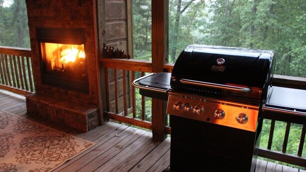 A wooden deck with a stone fireplace and a portable grill. - Beautiful Custom Cabin on almost 2 acres with lots of privacy (Blue Ridge)