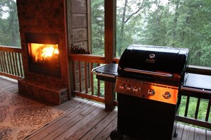 Une terrasse en bois avec une cheminée en pierre et un barbecue mobile.