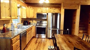 A wooden cabin interior with a kitchen featuring a stainless steel refrigerator, microwave, and oven, wooden cabinets, and a dining table with chairs. - Beautiful Custom Cabin on almost 2 acres with lots of privacy (Blue Ridge)