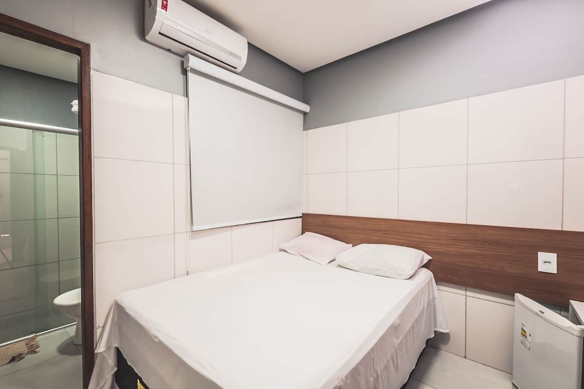 A hotel room with a bed, a wooden headboard, a white wall, and a window.
