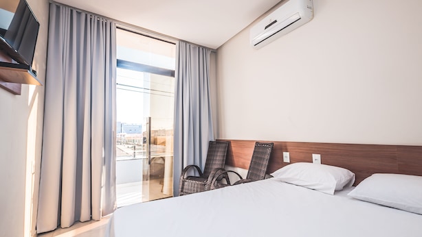 A hotel room with a bed, two chairs, a TV, and an air conditioning unit. - Hotel Imperial Palace (Bom Jesus Da Lapa)