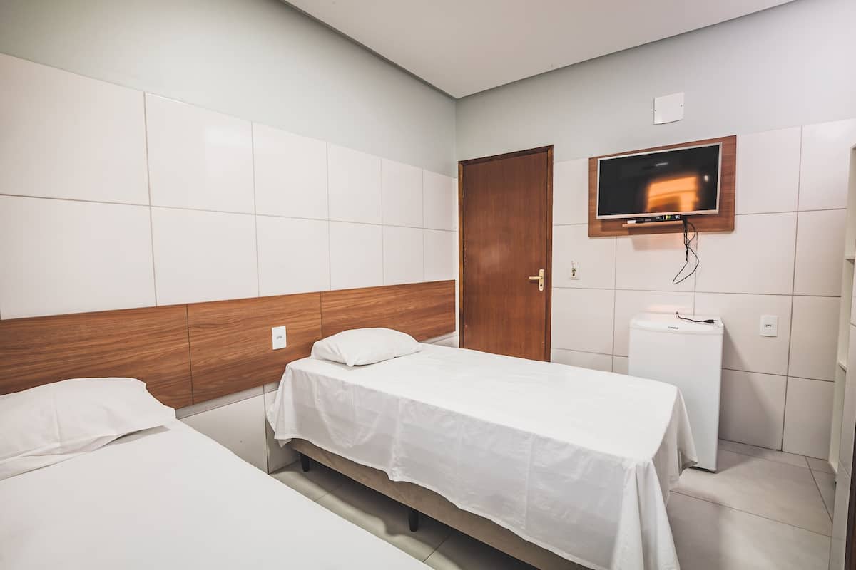 A hotel room with two beds, a TV mounted on the wall, and a small refrigerator.