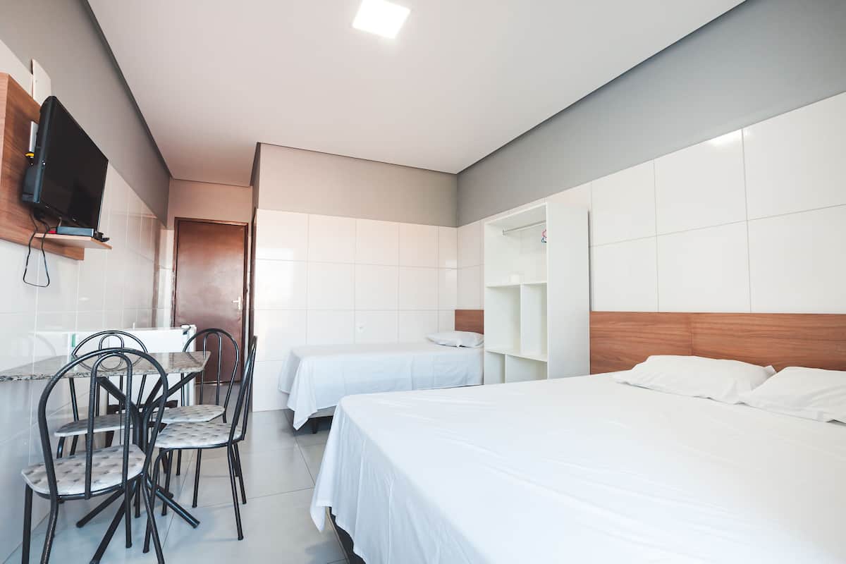 A hotel room with two beds, a dining area with chairs, a TV mounted on the wall, and a wooden headboard.