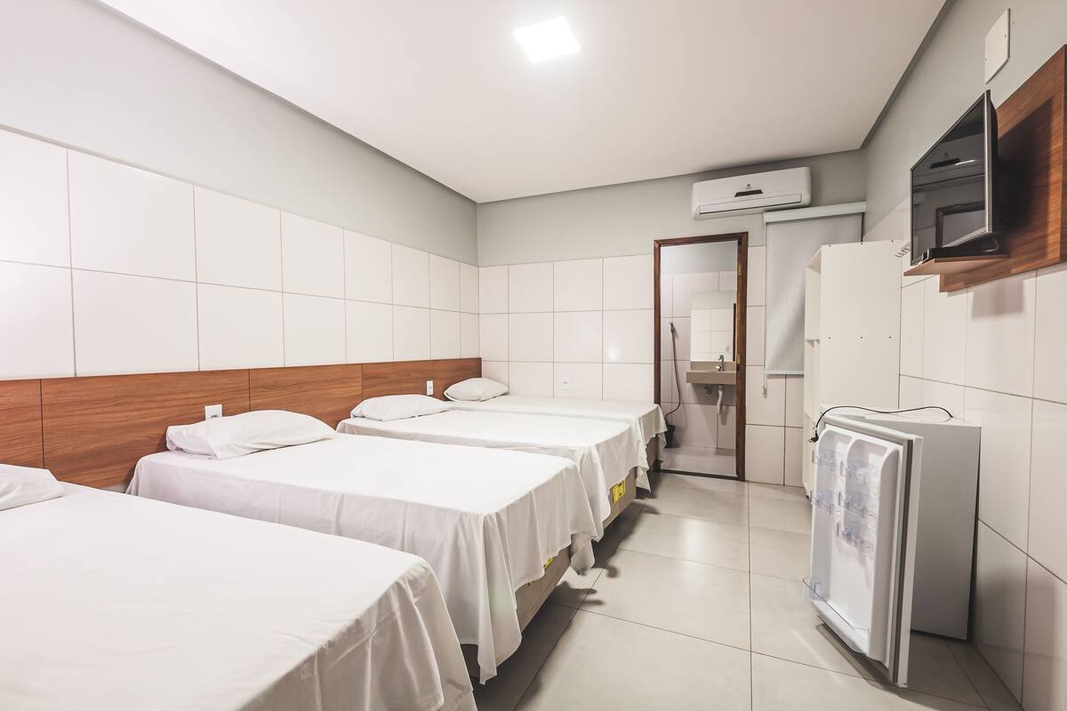 A hotel room with three single beds, a small kitchenette, and a water dispenser.