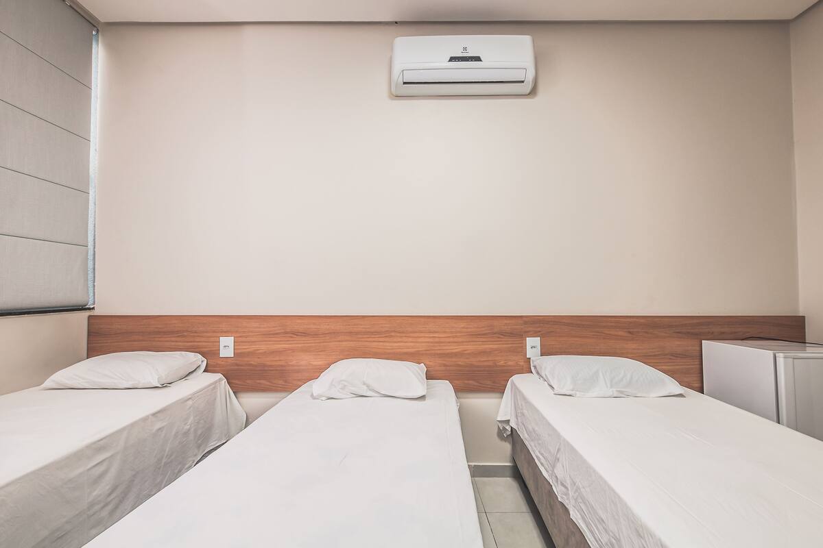 A hotel room with two single beds, a wooden headboard, an air conditioning unit, and a small desk.