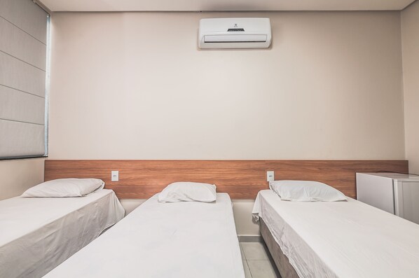 Una habitación de hotel con dos camas individuales, cabecero de madera, unidad de aire acondicionado y un pequeño escritorio.
