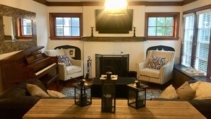 A cozy living room with a fireplace, two armchairs, a sofa, a piano, and a coffee table with candles. - Beautiful family home (Port Washington)