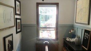 A staircase with a wooden handrail leading to a landing. There are framed pictures on the walls, a window with blinds, and a radiator below the window. - Beautiful family home (Port Washington)