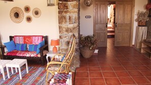 A cozy living area with a sofa, chair, and a table with a lamp. A stone wall and a wooden door are visible in the background. - EZKONBERRI VACATION RENTAL (Unzué)