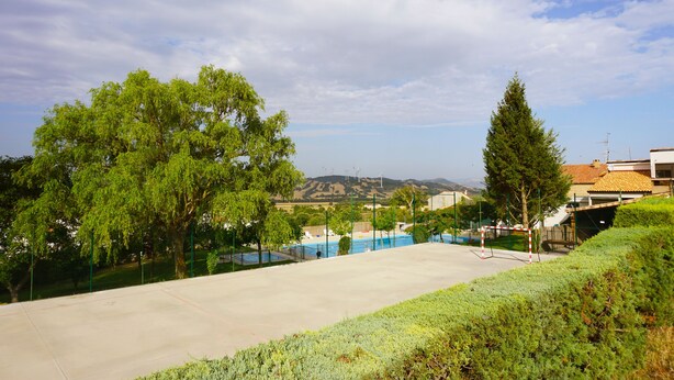 A tennis court with a net, surrounded by trees and a view of hills in the background. - EZKONBERRI VACATION RENTAL (Unzué)