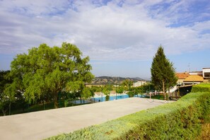 Un court de tennis avec un filet, entouré d’arbres, avec une vue sur des collines en arrière-plan.
