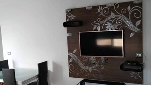 Un comedor moderno con una mesa de vidrio y sillas negras, un televisor montado en una pared decorativa y un mueble de entretenimiento negro debajo.