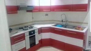 Una cocina compacta con armarios rojos y blancos, estufa a gas, un lavabo y una pequeña encimera.