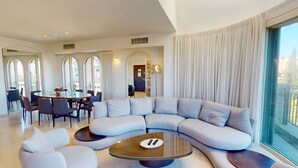 Ein modernes Wohnzimmer mit einer großen, bogenförmigen Eckcouch, einem Glastisch und einem Essbereich mit rundem Tisch und Stühlen.