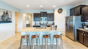 A modern kitchen with dark cabinets, a stainless steel refrigerator, and a granite countertop. - Solterra Sunshine - 5* - South facing large pool/spa - game room, gated resort (Davenport)