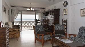 A room with a wooden cabinet, two patterned armchairs, a wooden table, and a view of the sea through a balcony. - LIDER, 4-D (Cullera)