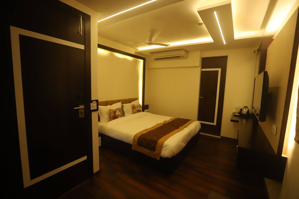 A hotel room with a bed, a ceiling fan, an air conditioning unit, a TV, and a door.