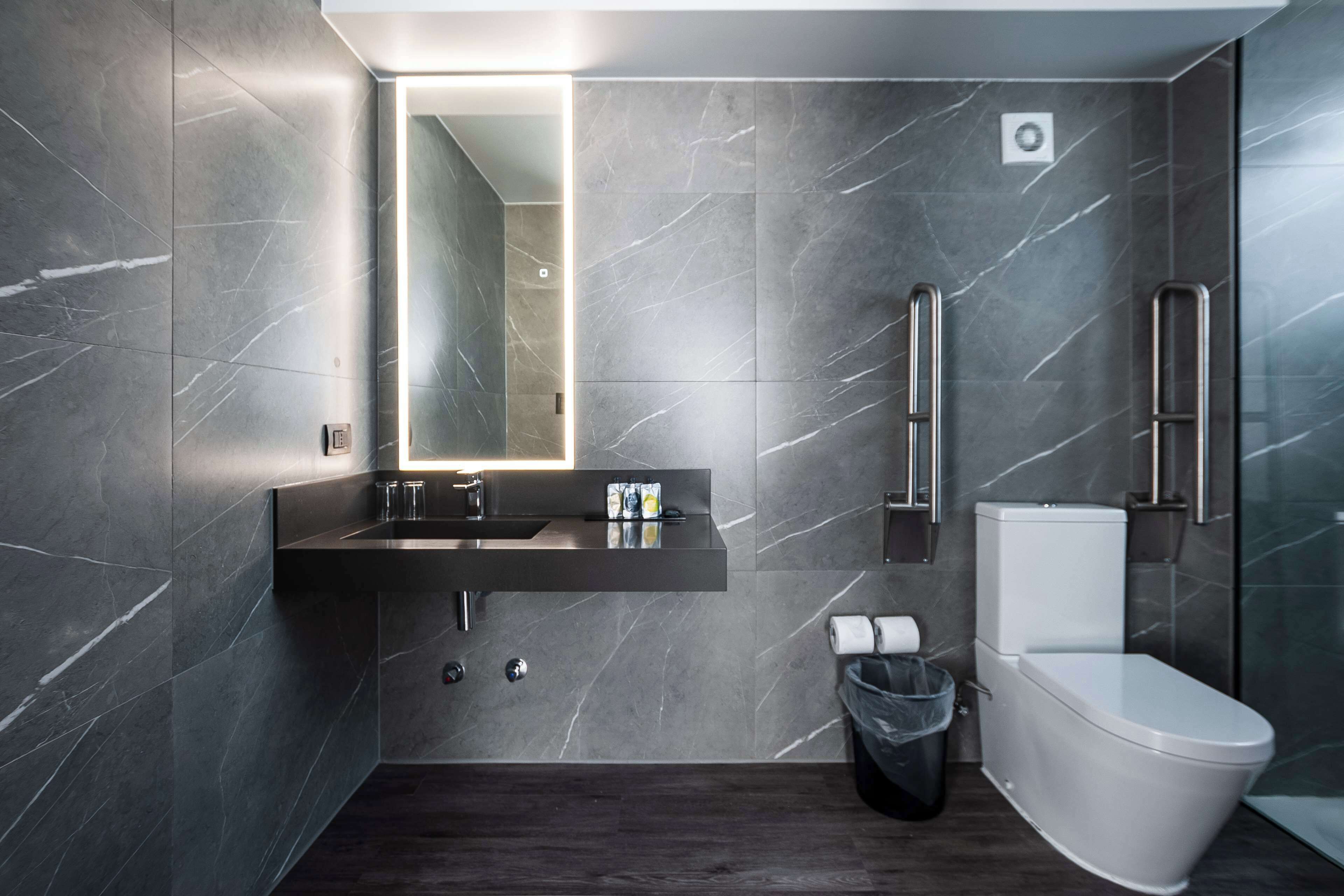 A modern bathroom with a dark marble wall, a built-in sink, a toilet, and a trash bin.