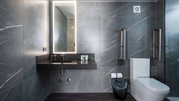 A modern bathroom with a dark marble wall, a built-in sink, a toilet, and a trash bin.