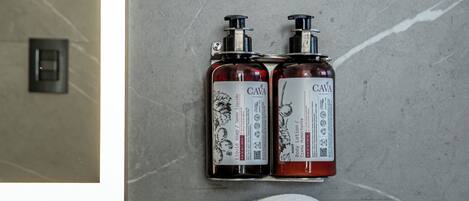 A bathroom with a marble wall, two CAVA body lotion bottles, and three rolled towels on a counter.