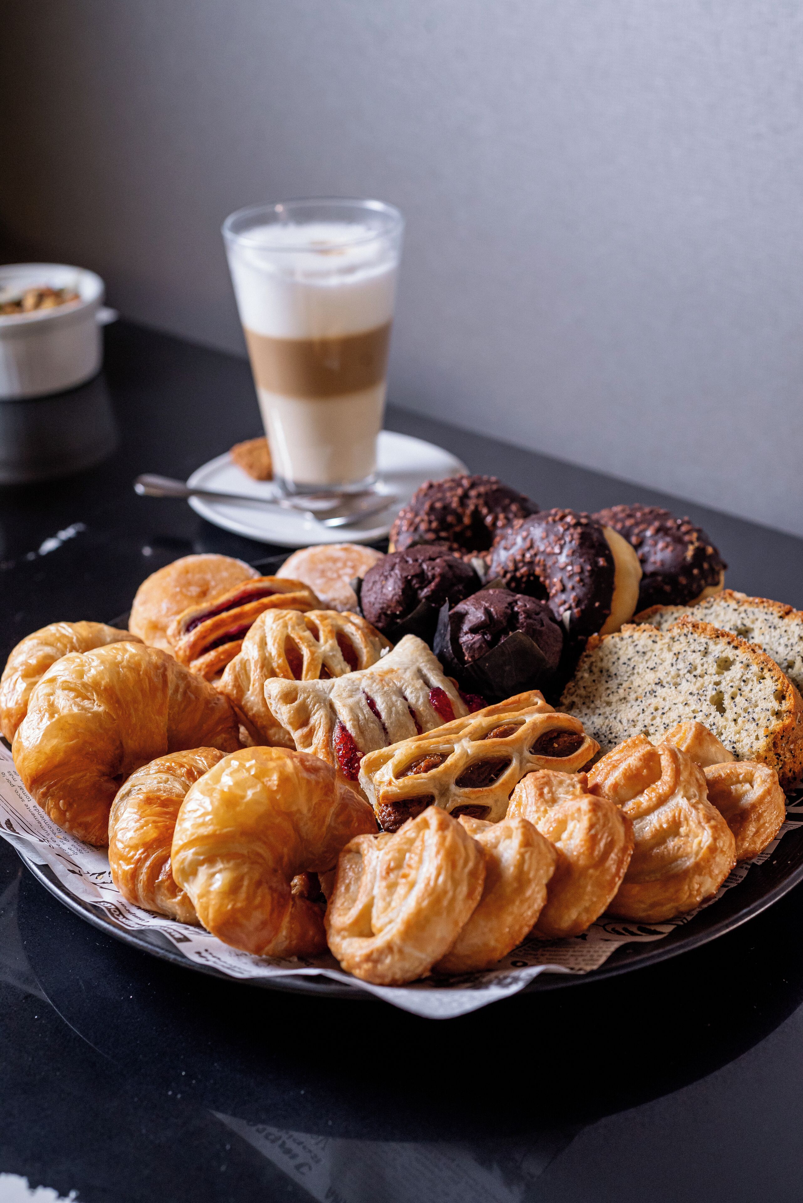 Un plat de pastissos variats i una tassa de cafè sobre una taula.