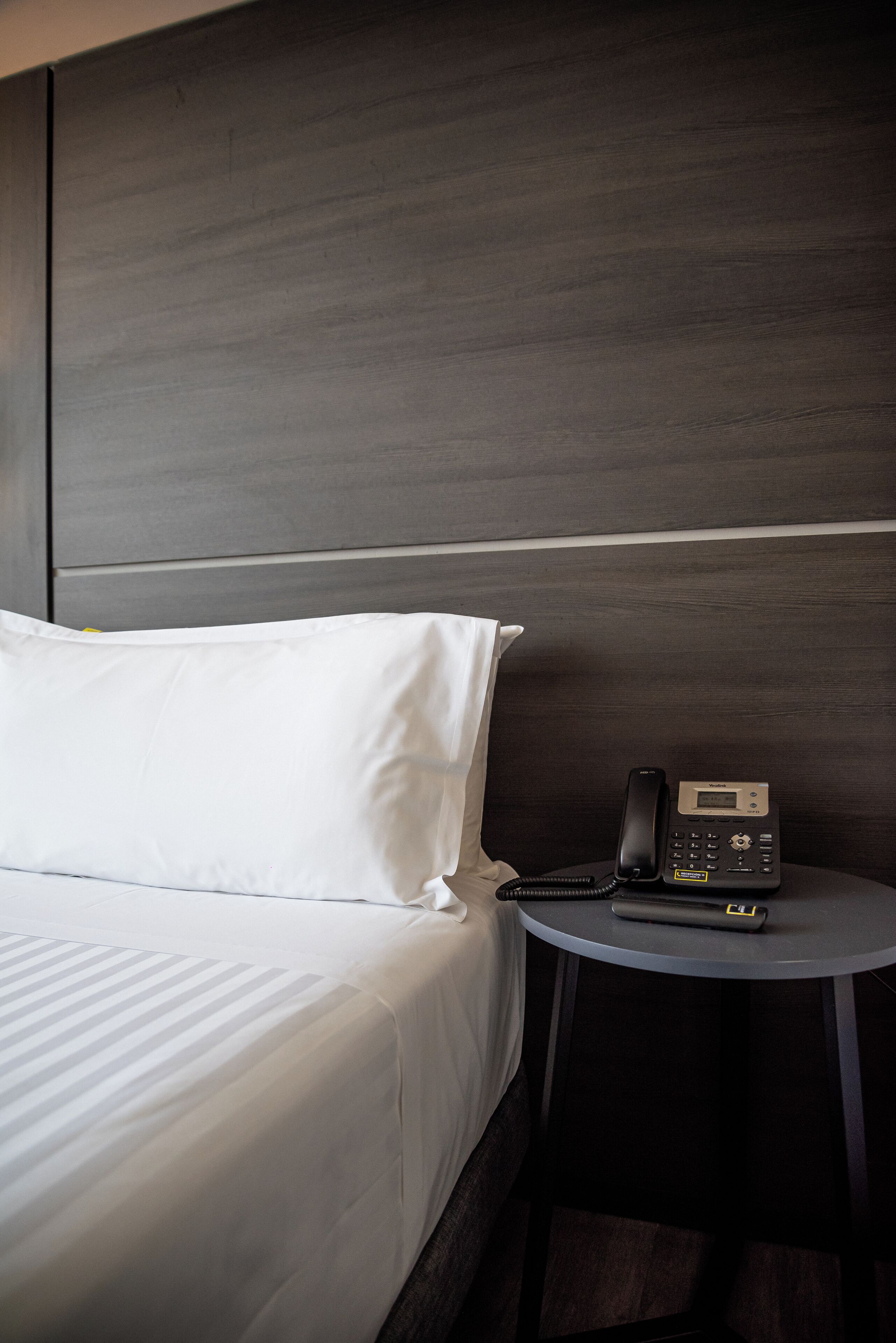 Une chambre d’hôtel avec un lit, une table de chevet avec un téléphone et une tête de lit.
