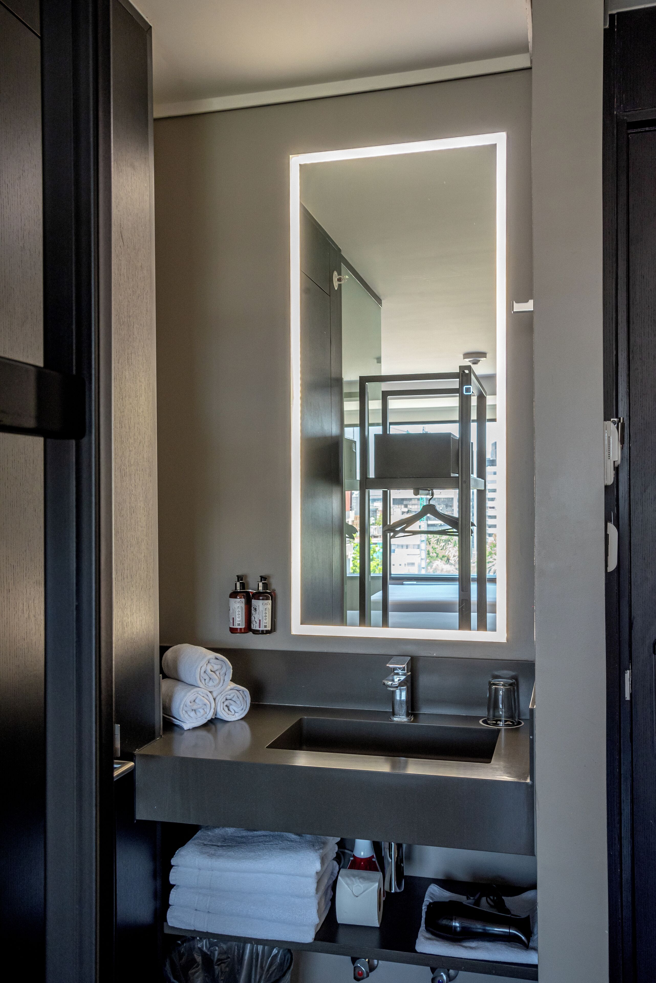 Un baño moderno con un espejo grande, un lavamanos y un perchero para toallas.