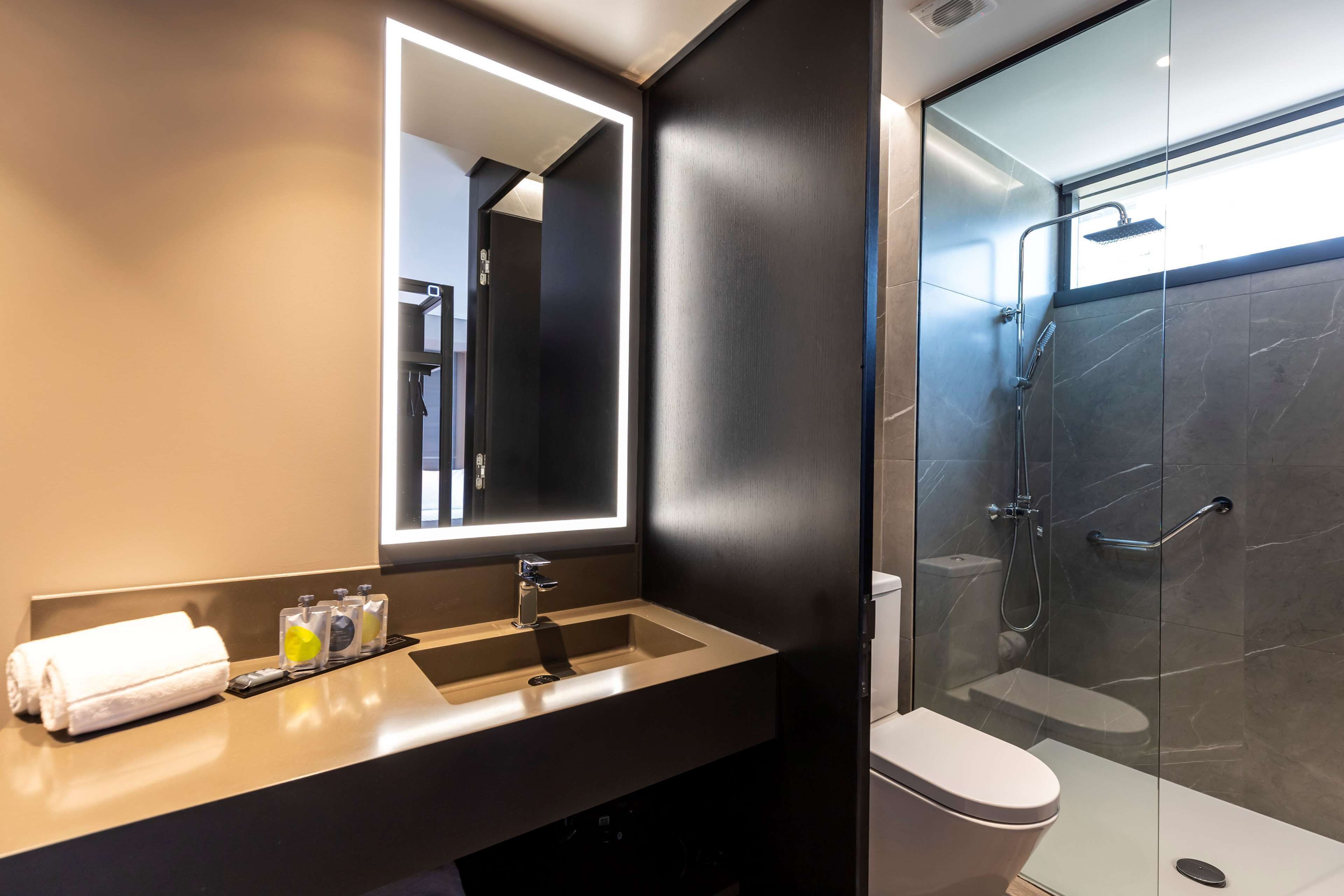 A modern bathroom with a large mirror, a sink, a toilet, and a glass-enclosed shower.