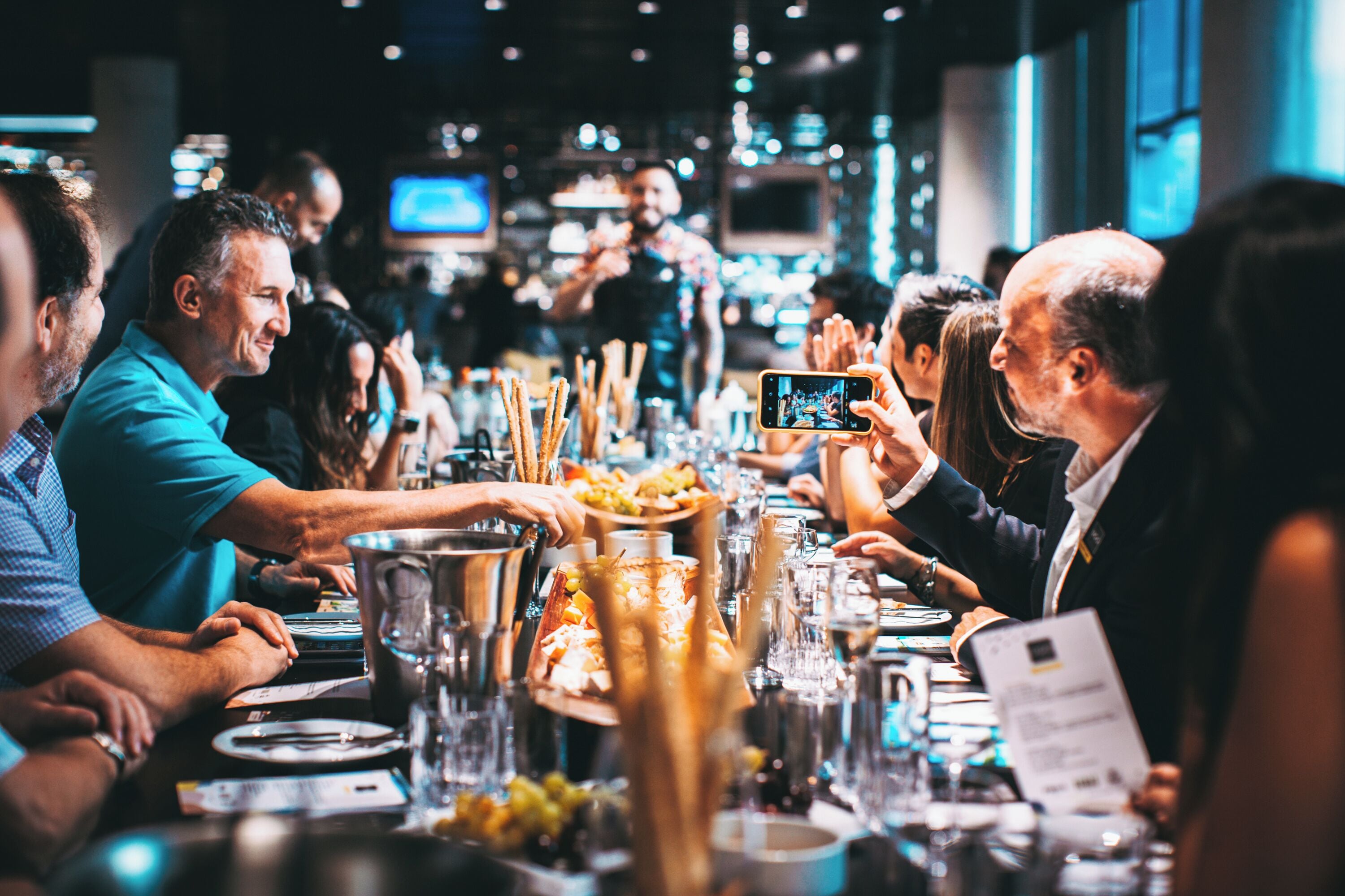 A group of people dining at a restaurant with a long table, glasses, and a variety of dishes.