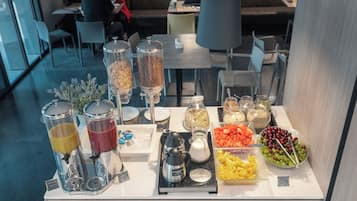 Montaje de bufé con diversas opciones de comida y bebida, entre ellas frutas, cereales y refrescos.