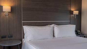 A hotel room with a large bed, two bedside lamps, a small round table, and a telephone on the nightstand.