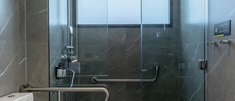 A modern bathroom with a glass-enclosed shower, a toilet with a handrail, and a visible window.