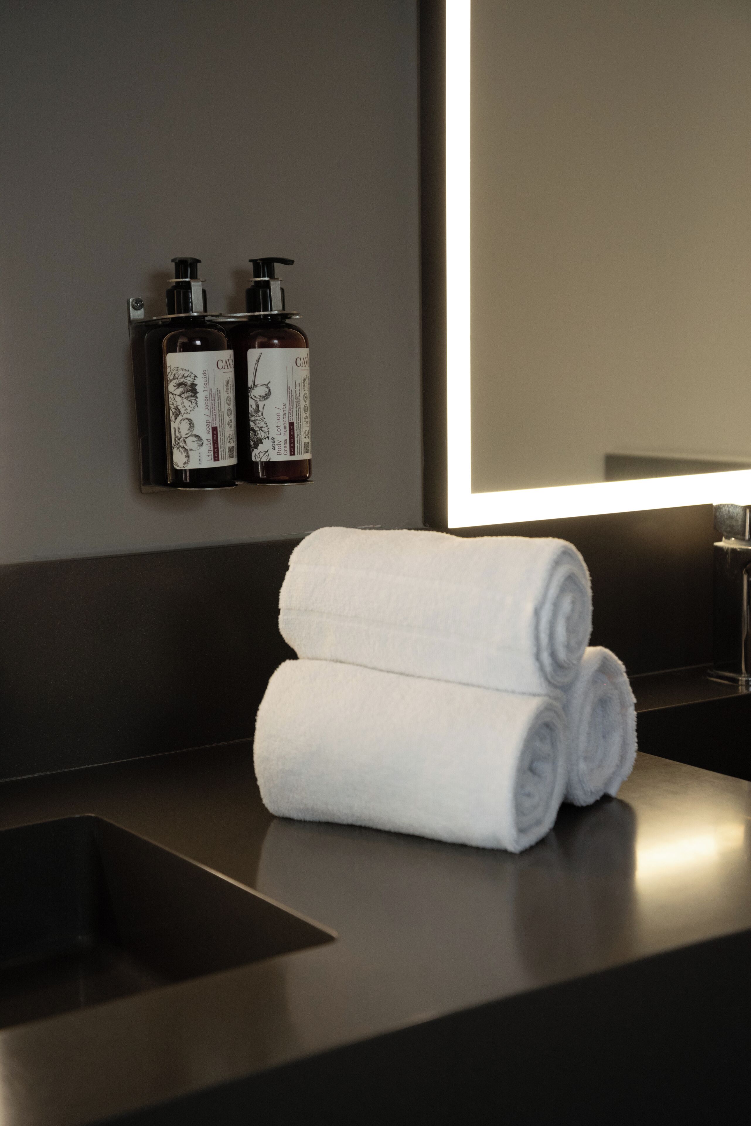 A bathroom with a dark countertop, a mirror, and two bottles of lotion.