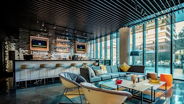 A modern bar area with a bar counter, stools, and a seating area with sofas and a coffee table.