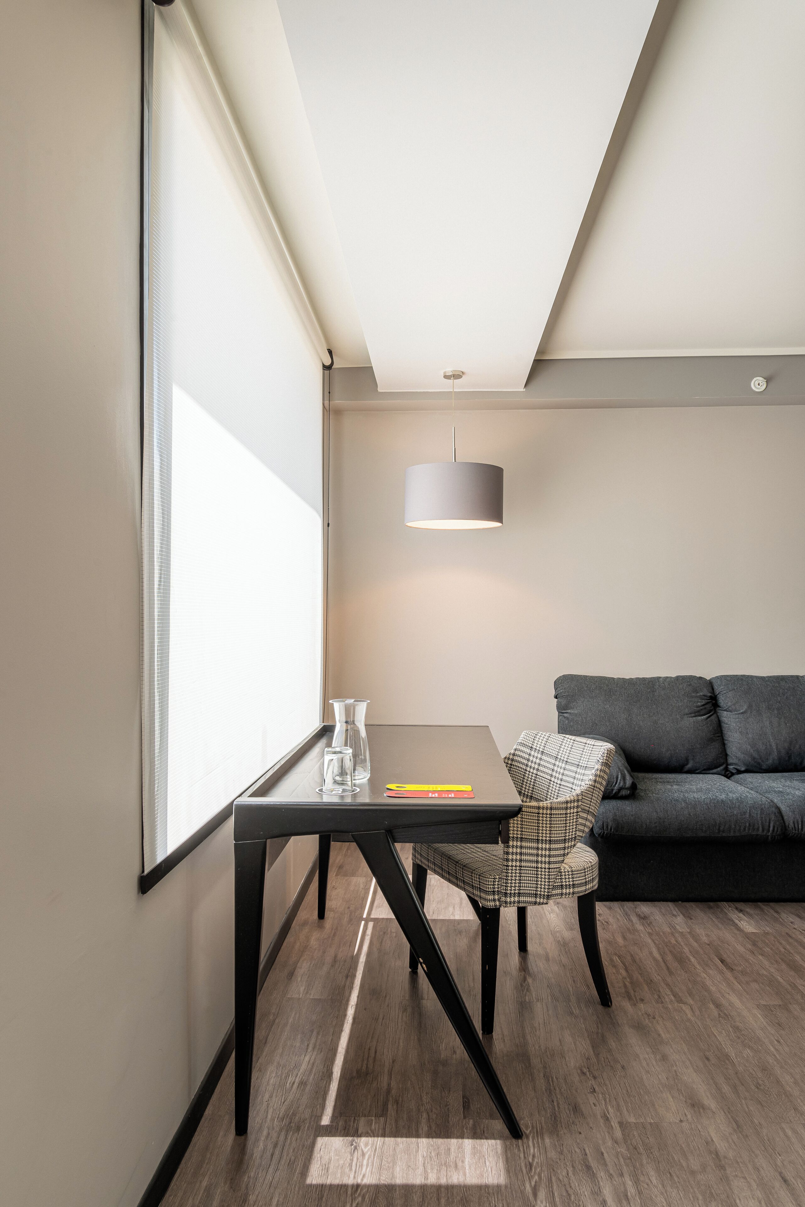 Ein modernes Zimmer mit einem dunkelgrauen Sofa, einem kleinen Tisch mit einer Glasvase und einem karierten Stuhl.