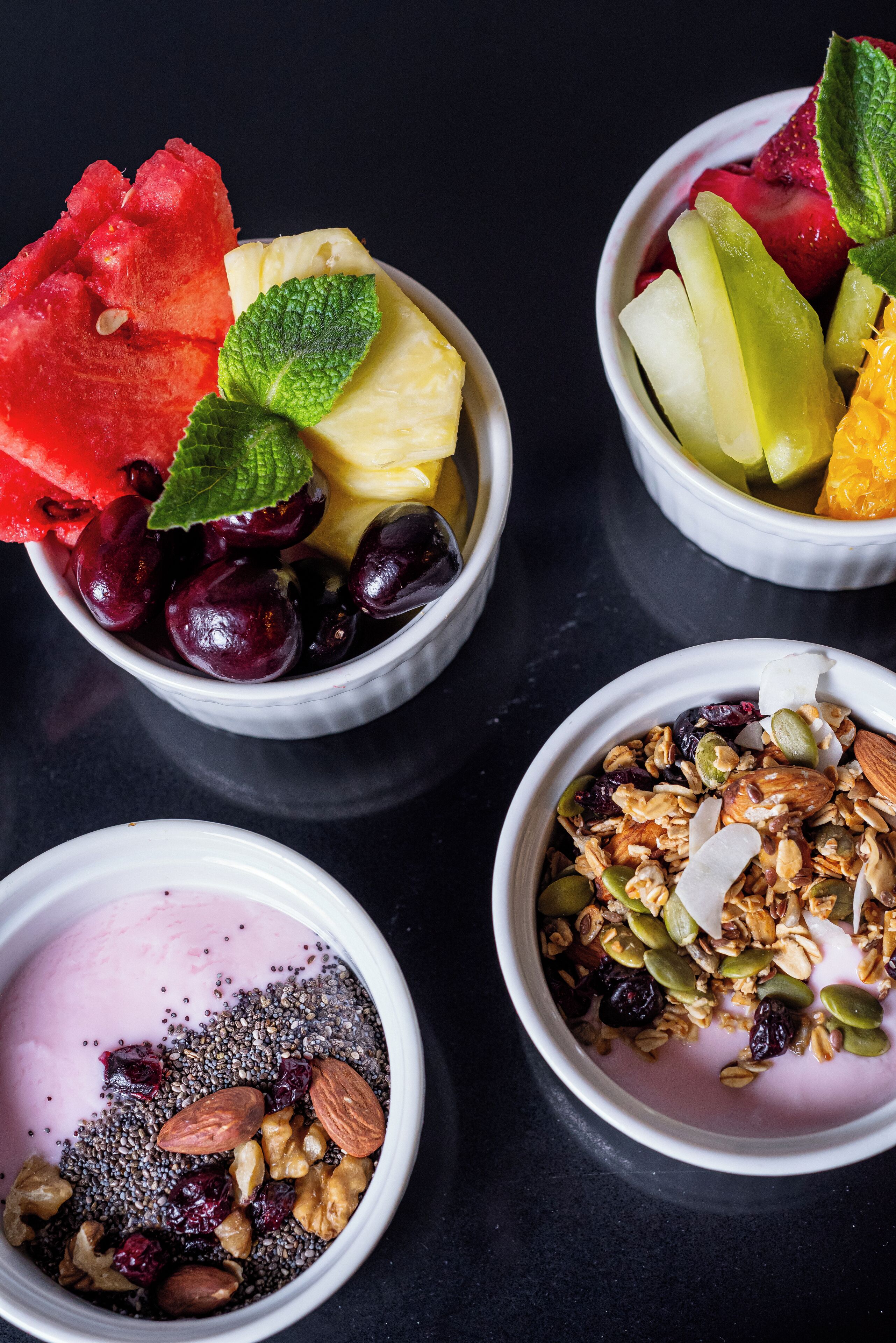 Four bowls of various fruits and granola.