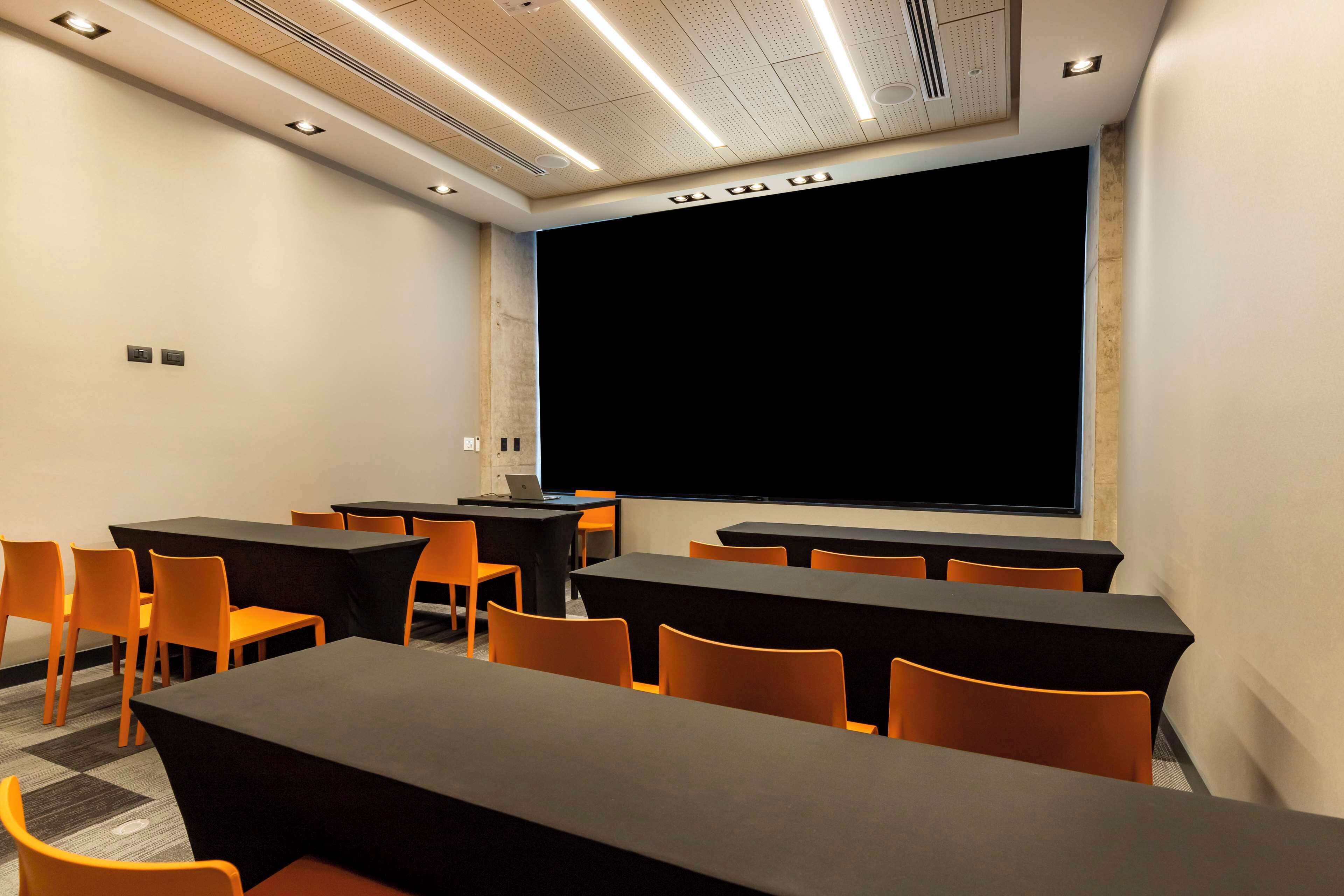 A conference room with tables and chairs, a projector screen, and a laptop on a table.