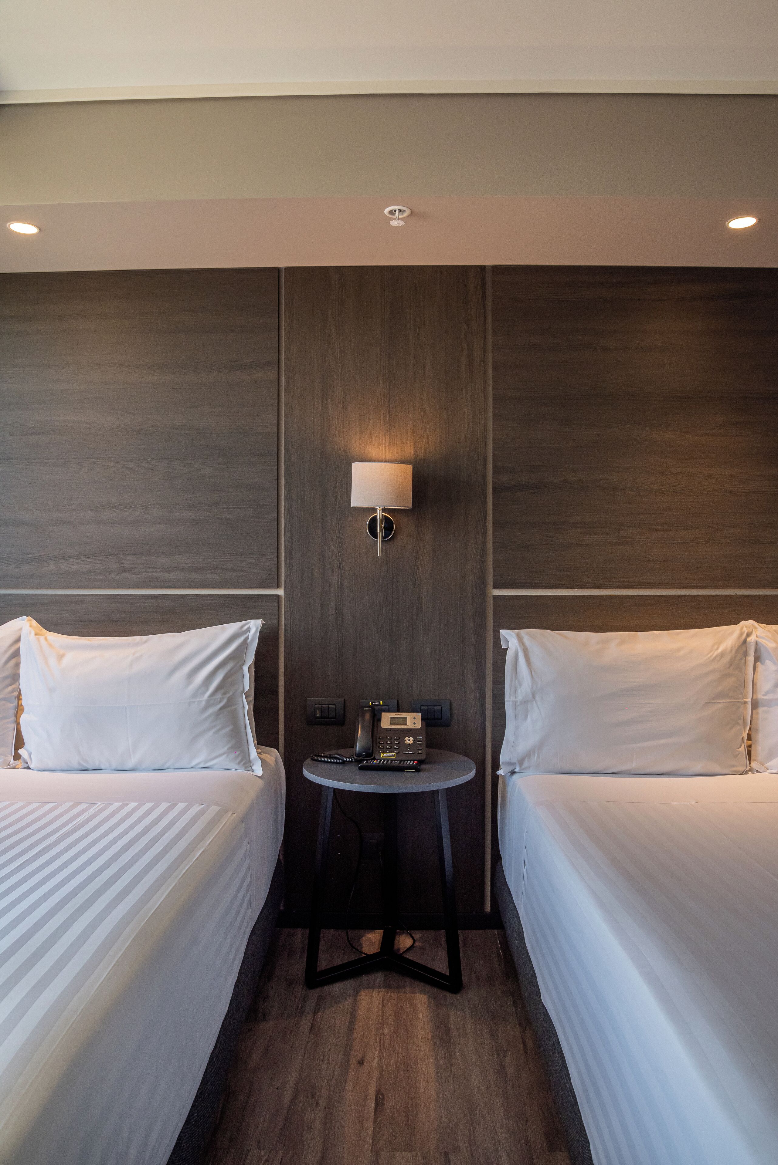 A hotel room with two single beds, a small table with a lamp, and a telephone.